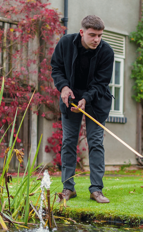 Man in black jacket cleaning garden pond with a net.
