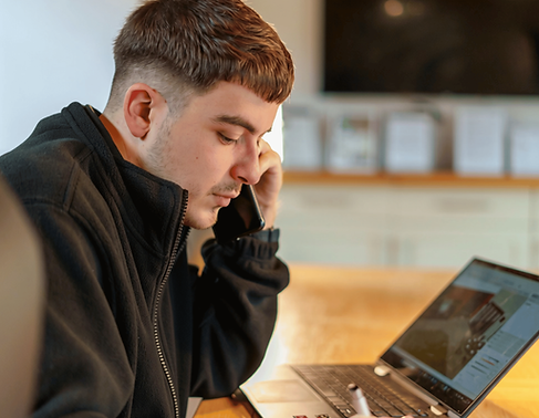 Young man talking on a smartphone while using a laptop.