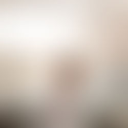 Pregnant Single Mom by Choice  in a white dress smiles by the ocean at sunset. Rocky shore, gentle waves, and warm, serene atmosphere.