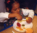 A young girl cuts a banana and other pieces of fruit