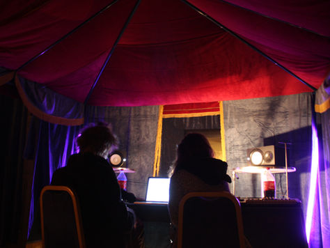 Audio engineers working at a workstation inside a red and blue tent structure.