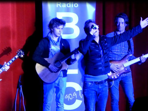 Live band performing on a stage with a singer and guitarists under blue lights.
