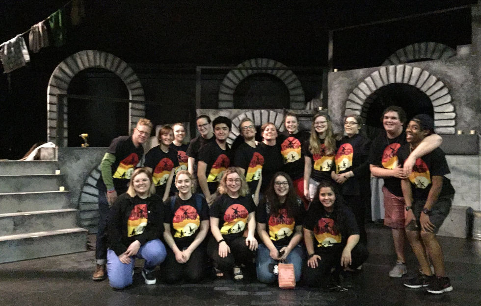 The Cast and Crew in matching show shirts pose in front of the set that looks like a deep dungeon for The Man of La Mancha