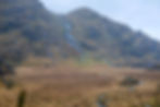 Small waterfall coming down a rocky mountainside into damp wet fields of bog