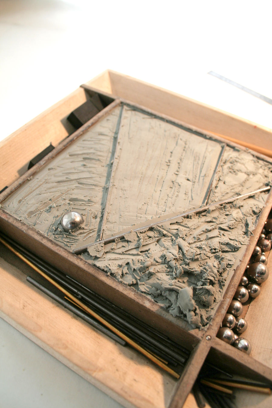 CLAY WITHIN A FRAME TEXTURED TO CREATE AN ABSTRACT LANDSCAPE. BALL BEARINGS REST IN A PERIMETER TROUGH WAITING TO BE INTRODUCED TO THE LANDSCAPE.