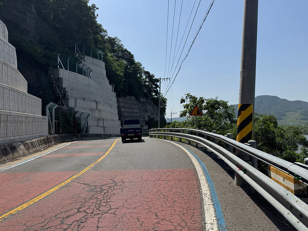 A car drives along a winding mountain road under a clear blue sky.