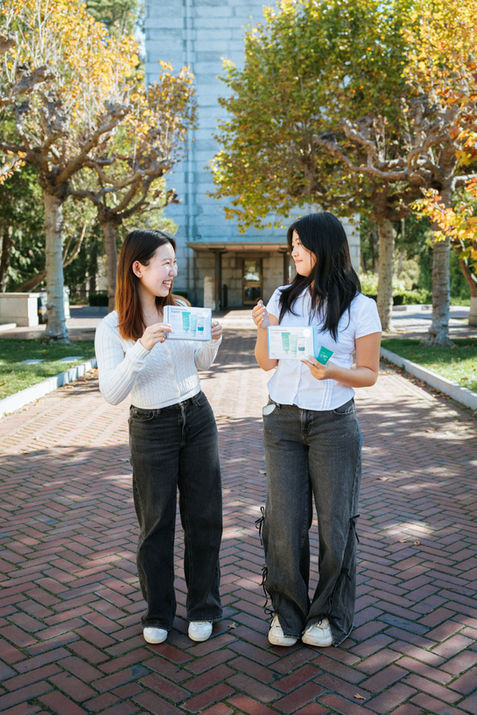 Two people holding products outdoors, smiling at each other.