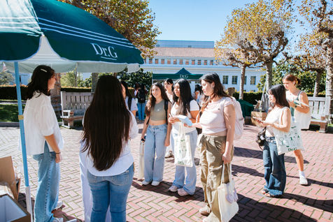 Group of people gathered outdoors under green canopy.
