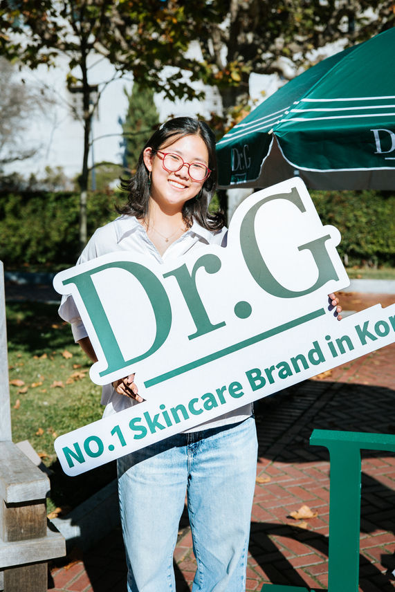 Person holding "Dr.G" skincare brand sign outdoors.