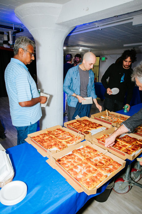 People serving themselves pizza from boxes on a table.