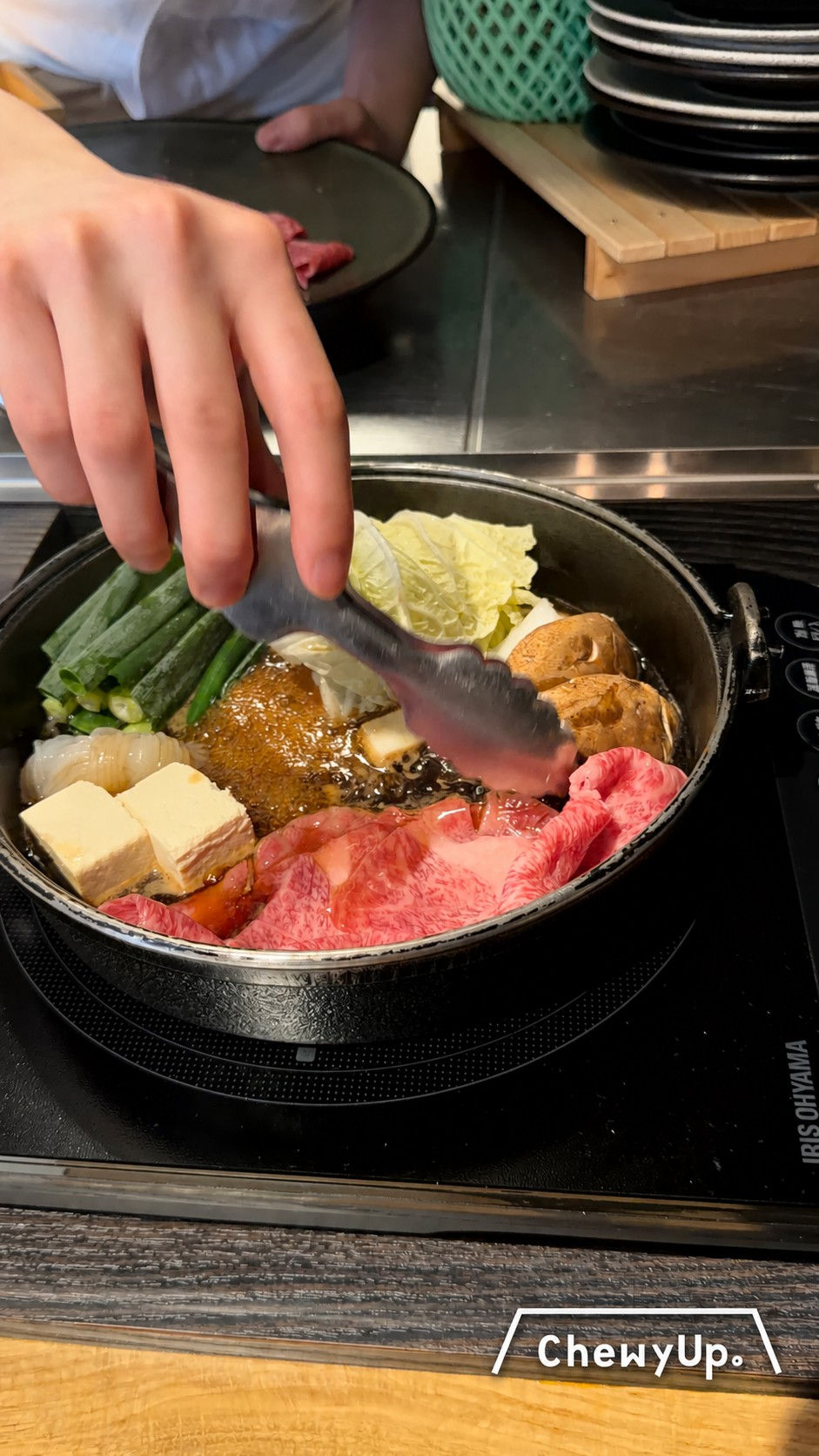 店員在面前烹調壽喜燒,鍋內有牛肉、豆腐和蔬菜。