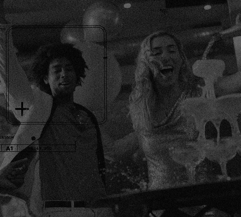 grainy image of a live performance or speaking event, showing a person on stage with a blurred audience in the background