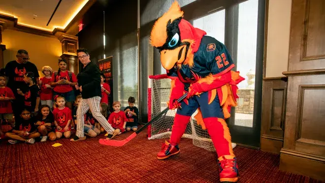 Cardinal mascot holding a hockey stick with children around.