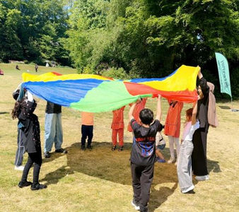 Children play in a park on a warm day. They are holding a multicoloured flag and having a game with it.