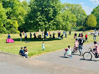 Children play in a park on a warm day. Children are gathered on bikes and playing ball games.