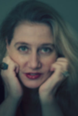 Potrait of Tabatha Stirling: long blonde hair and red lipstick, her face resting on her hands that have large rings