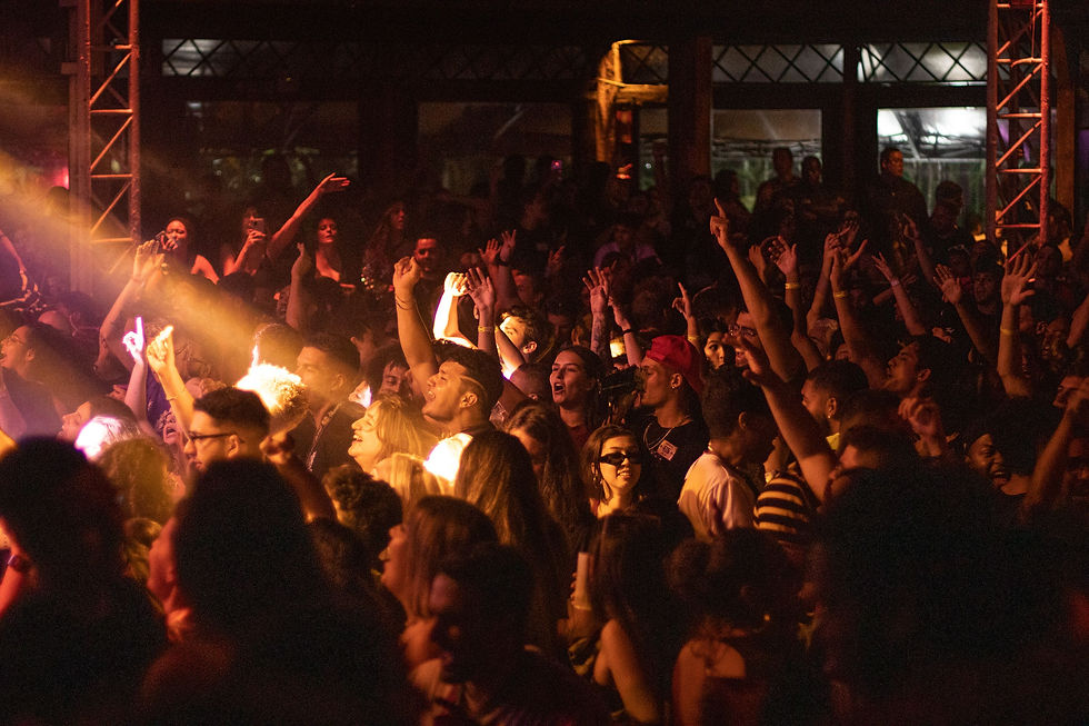 Crowded concert audience with raised hands under warm orange stage lights in a dark indoor venue, energetic and celebratory