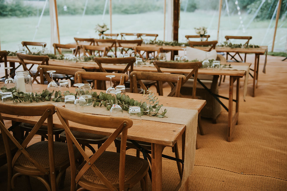 Wide rustic trestle tables in a Peacock and Bow pole and canvas marquee.