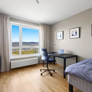 En pult med laptop på, seng i hjørnet og fantastisk utsikt ut av vinduet.