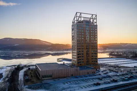 Stort tårn i tre som ligger ved et vann i solnedgang.