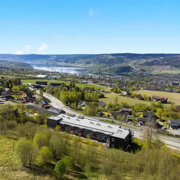Dronefoto av et leilighetsbygg i Lillehammer hvor man kan se bykjernen og Mjøsa i bakgrunnen.