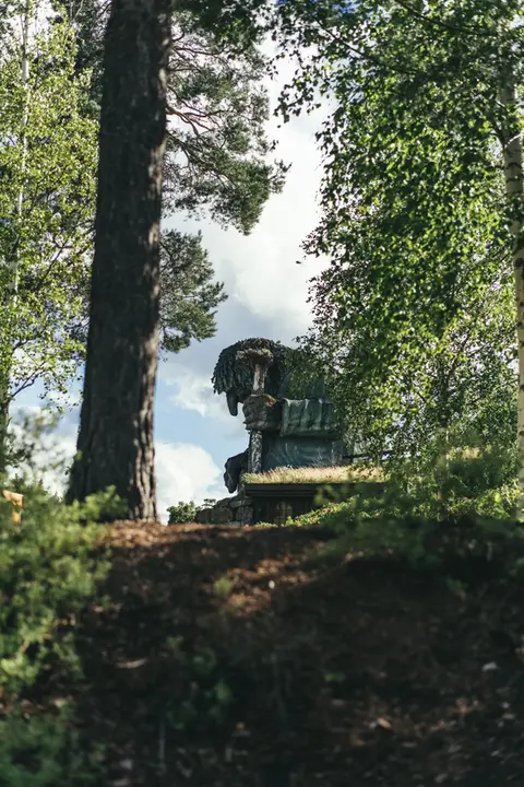 Path through a forrest with the statue of a big troll sitting in the end.