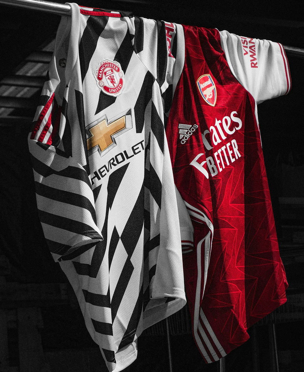 Two soccer jerseys, Manchester United (black/white) and Arsenal (red), hang side by side on a rod in a dark setting, showcasing logos.