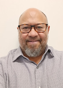 Jose Montero, member of the Art House's board. He is wearing a white shirt and glasses in front of a plain background.