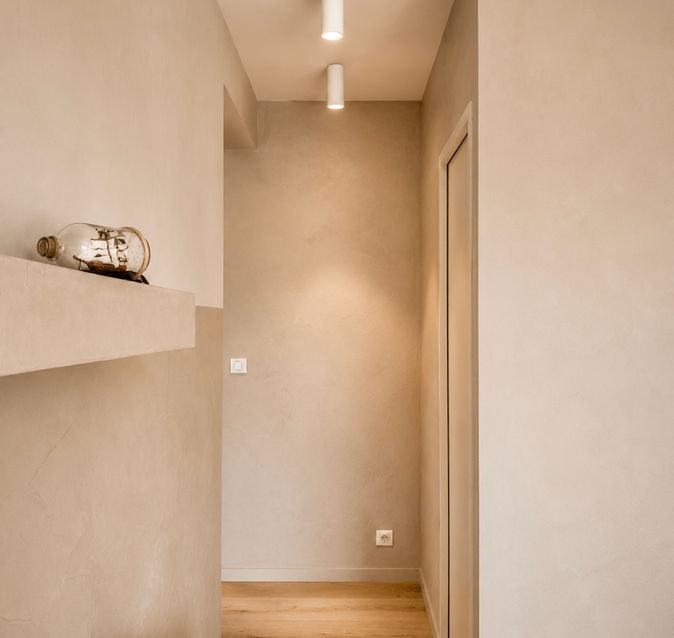 Couloir aux enduits minéraux et parquet en chêne, baigné d'une lumière douce, illustrant une rénovation sobre, chaleureuse et intemporelle réalisée en Corse-du-Sud.