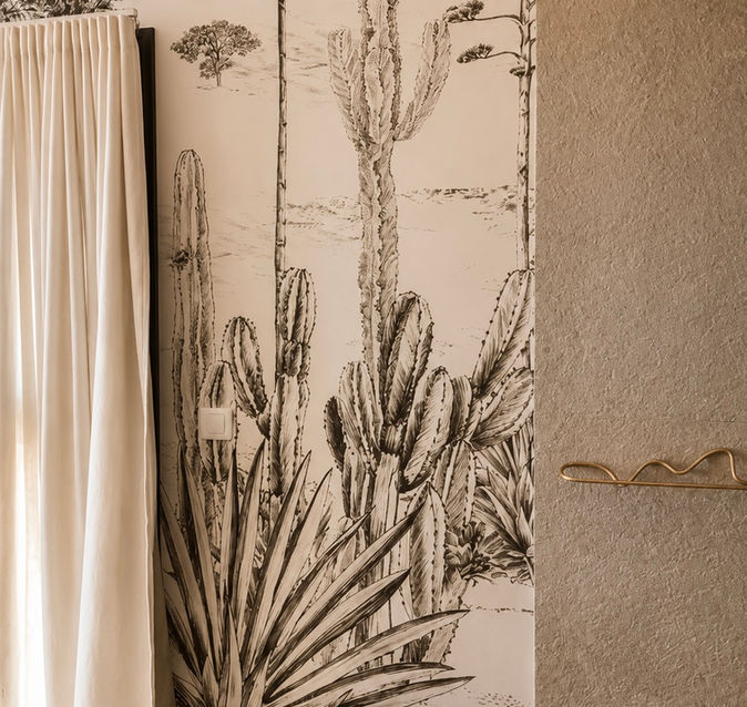 Papier peint panoramique illustré aux inspirations méditerranéennes et désertiques, associé à des matériaux minéraux et des finitions chaleureuses dans une salle de bain contemporaine.