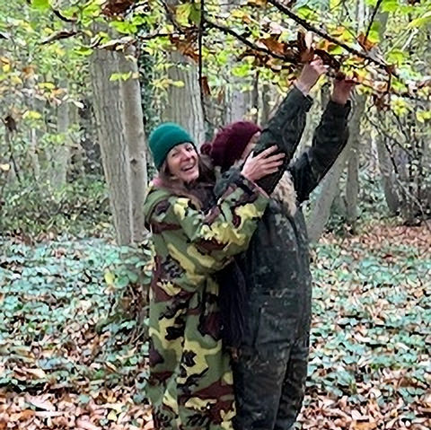 Two people on a forest therapy walk, reaching for branches.