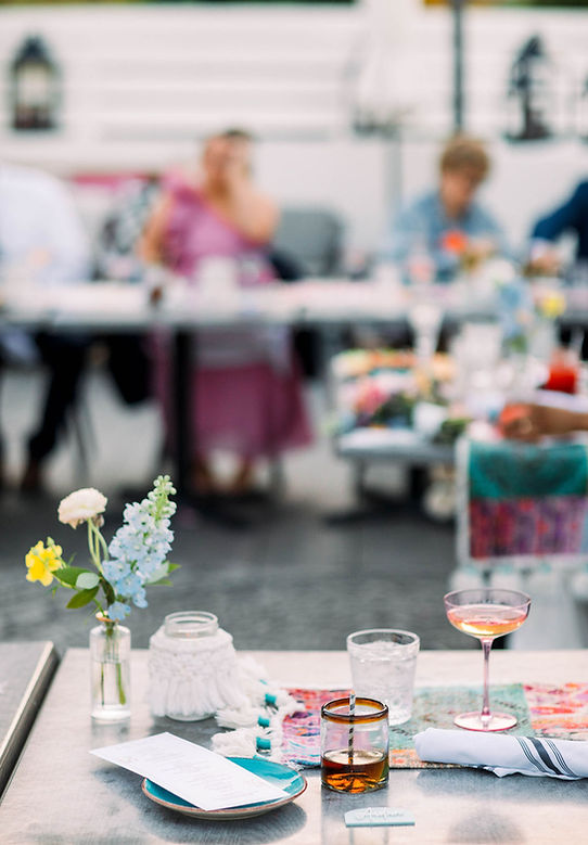 a dining table with flowers, glasses, and plates set for a meal with people in the background