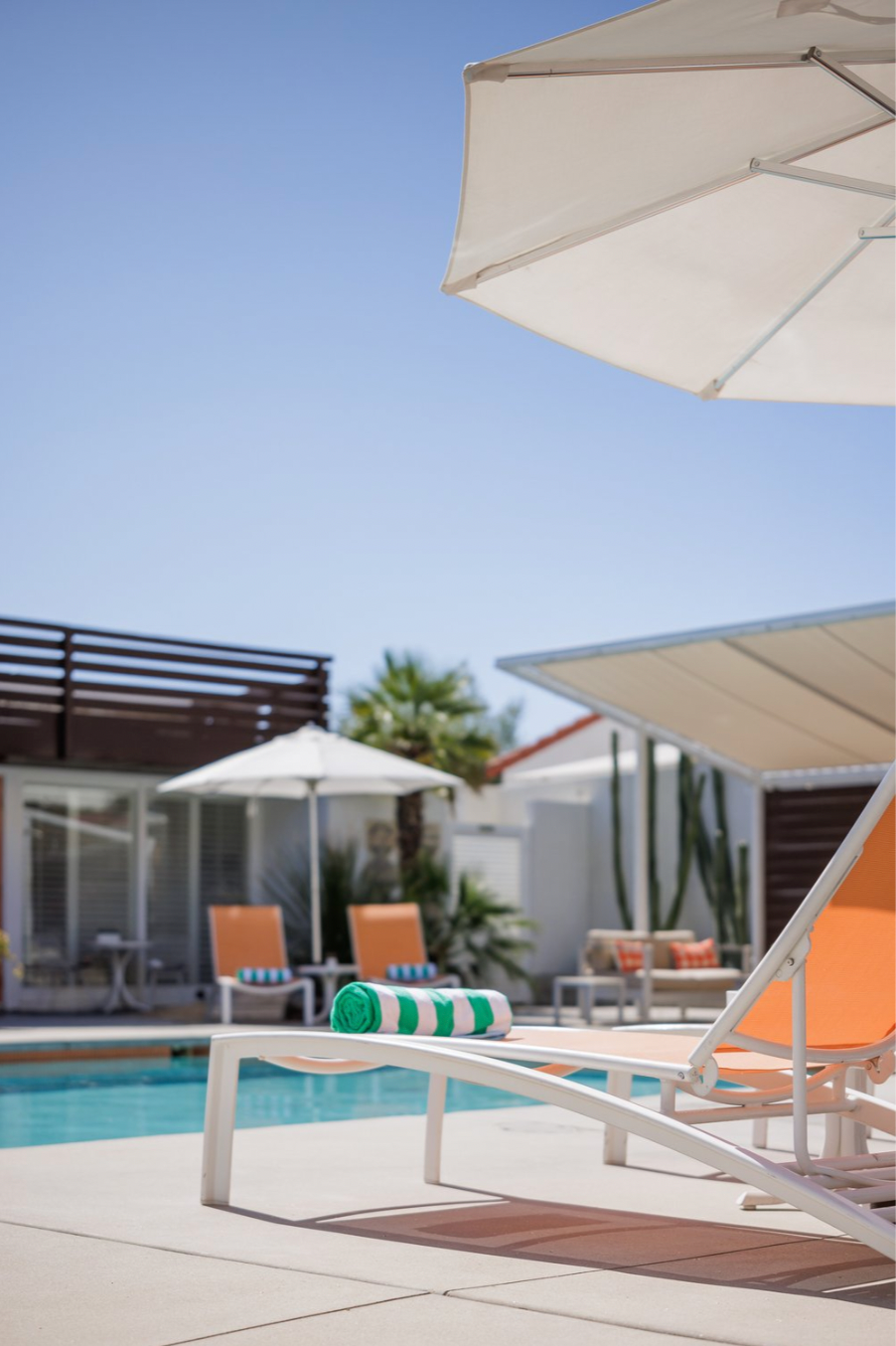 A poolside scene with lounge chairs, umbrellas, and a pool under a clear blue sky.