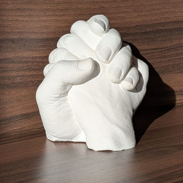 white plaster cast of adult hands on dark brown background
