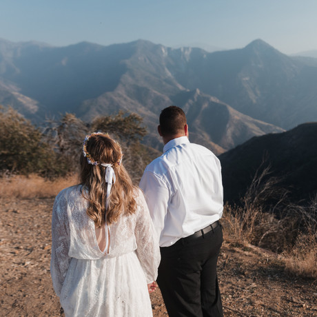 Destination wedding in Sequoia National park with a bride and groom in white and black with a flower crown overlooking a mountain landscape