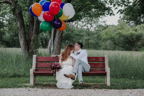 Bride and groom with colorful balloons in Pennypack Park in Philadelphia. Bold pink bouquet on a bench in springtime