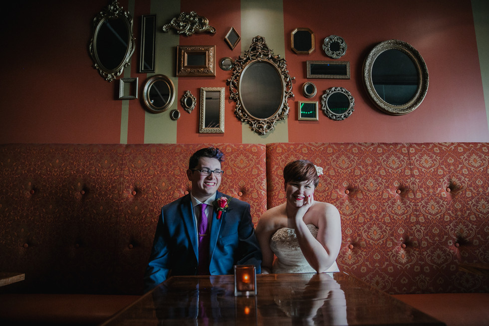 Bride and groom in bold colors in front of an orange wall of mirrors in Lancaster PA restaurant. The groom has a purple tie and blue suit and the bride has a flower in her hair and pink bouquet