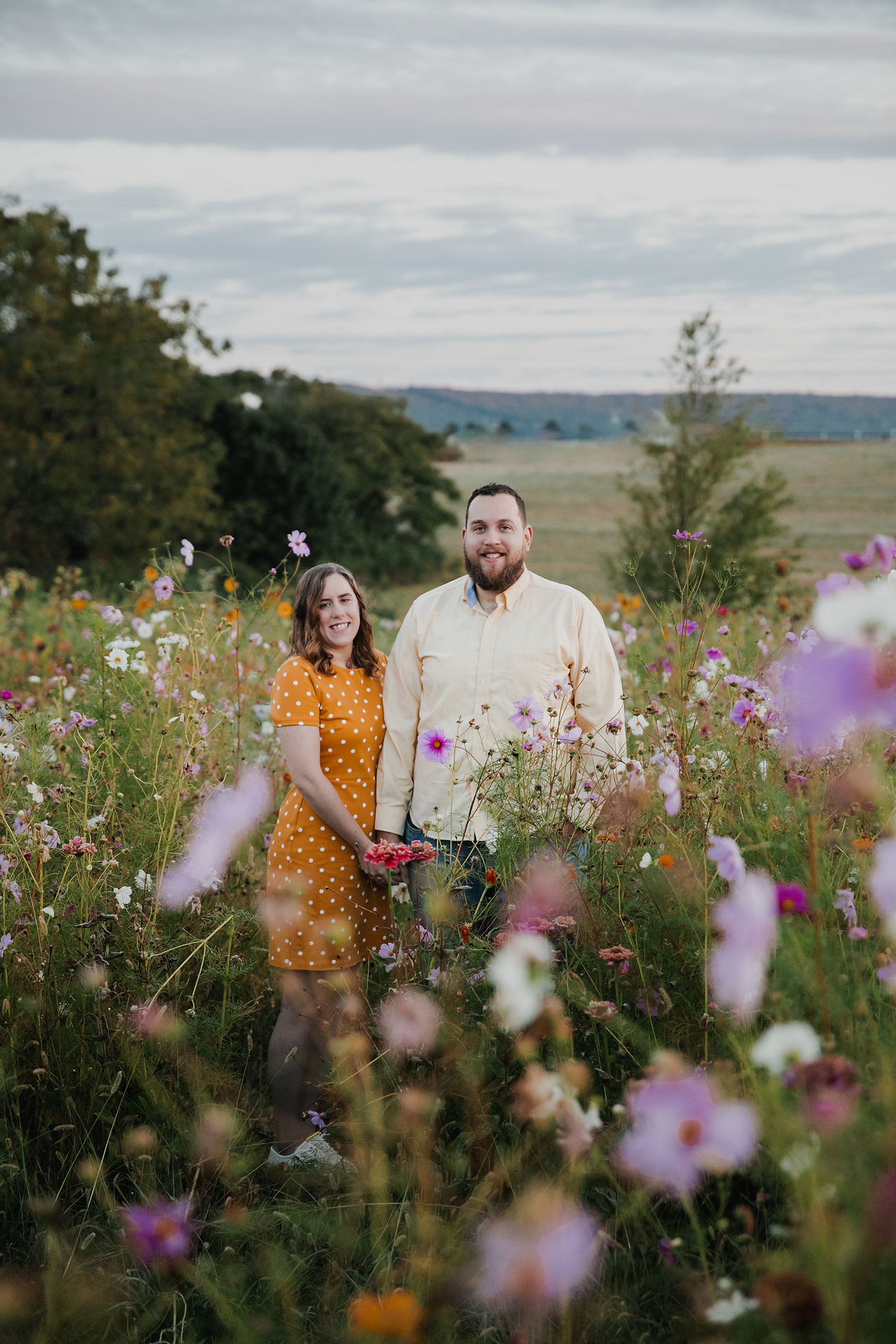 Engagement session in a wildflower field with the bride wearing a yellow polkadot dress and the groom in a yellow shirt at sunrise