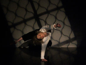 A dancer in a balance on one and and leg, the other two stretched out twisting their body. Light from a window highlights then in the space.