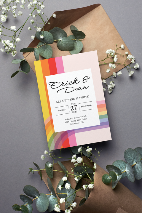 Wedding invitation featuring rainbow graphic elements and elegant typography, displayed on a gray surface with eucalyptus leaves, white flowers, and kraft paper envelopes, creating a modern and romantic flat-lay composition.