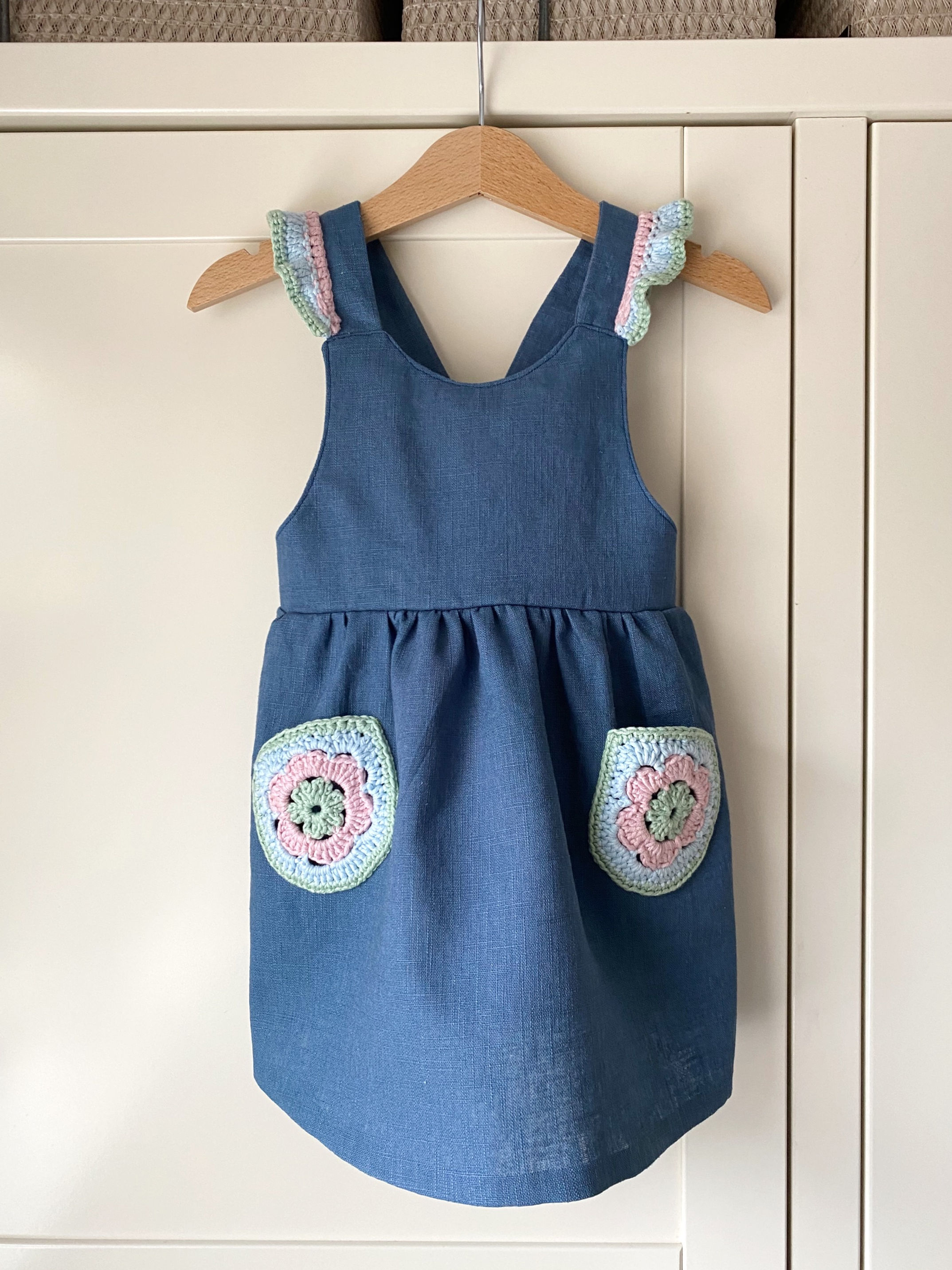 Navy blue linen children's pinafore dress with crochet frill straps and crochet flower pockets by Little Fig