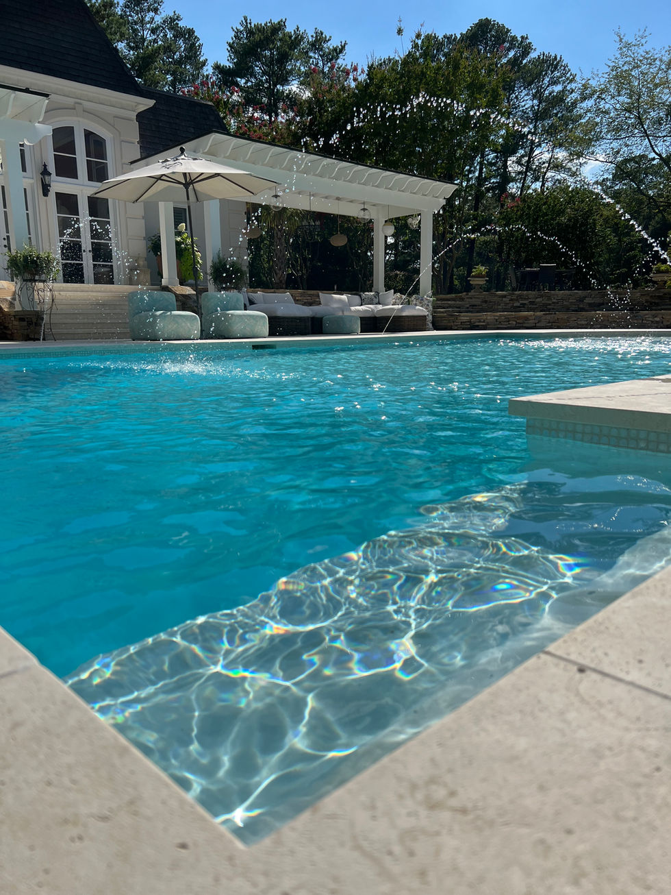 a large swimming pool with a pergola and umbrella in the background