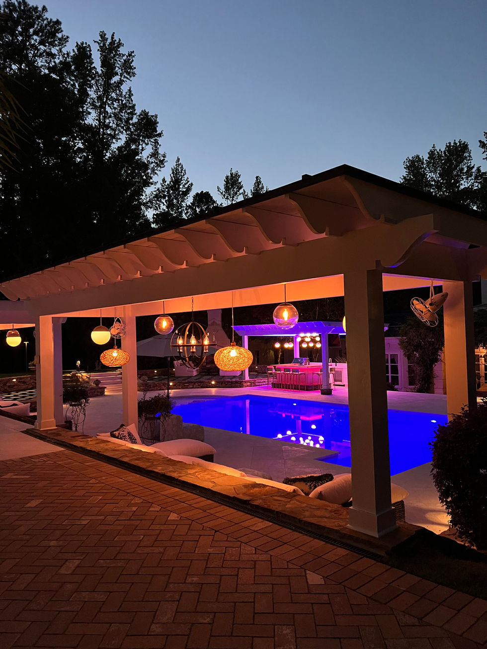 a large swimming pool is lit up at night under a pergola