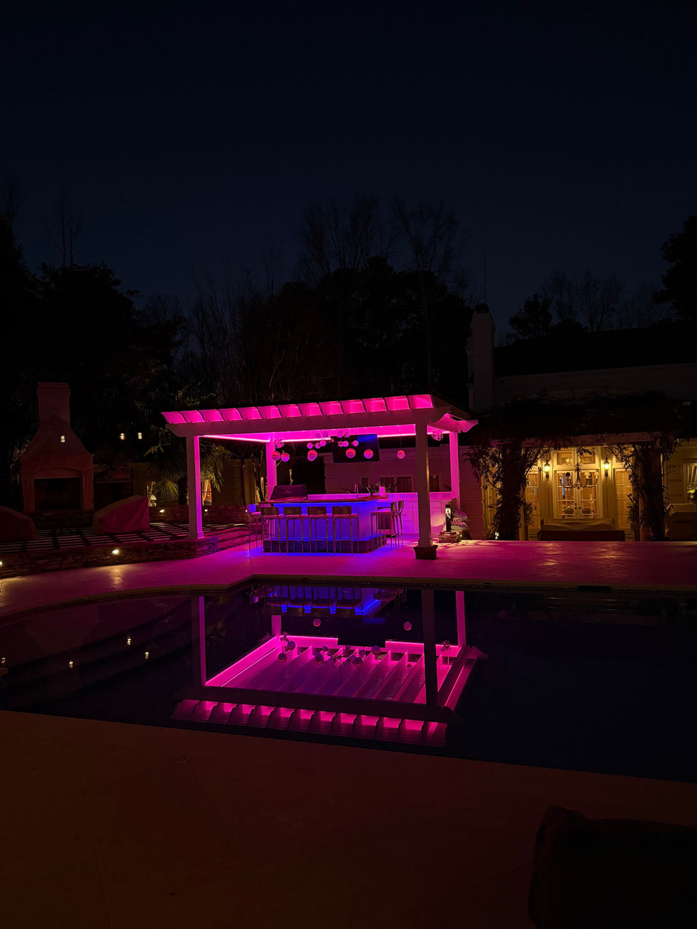 a swimming pool with a bar under a pergola at night