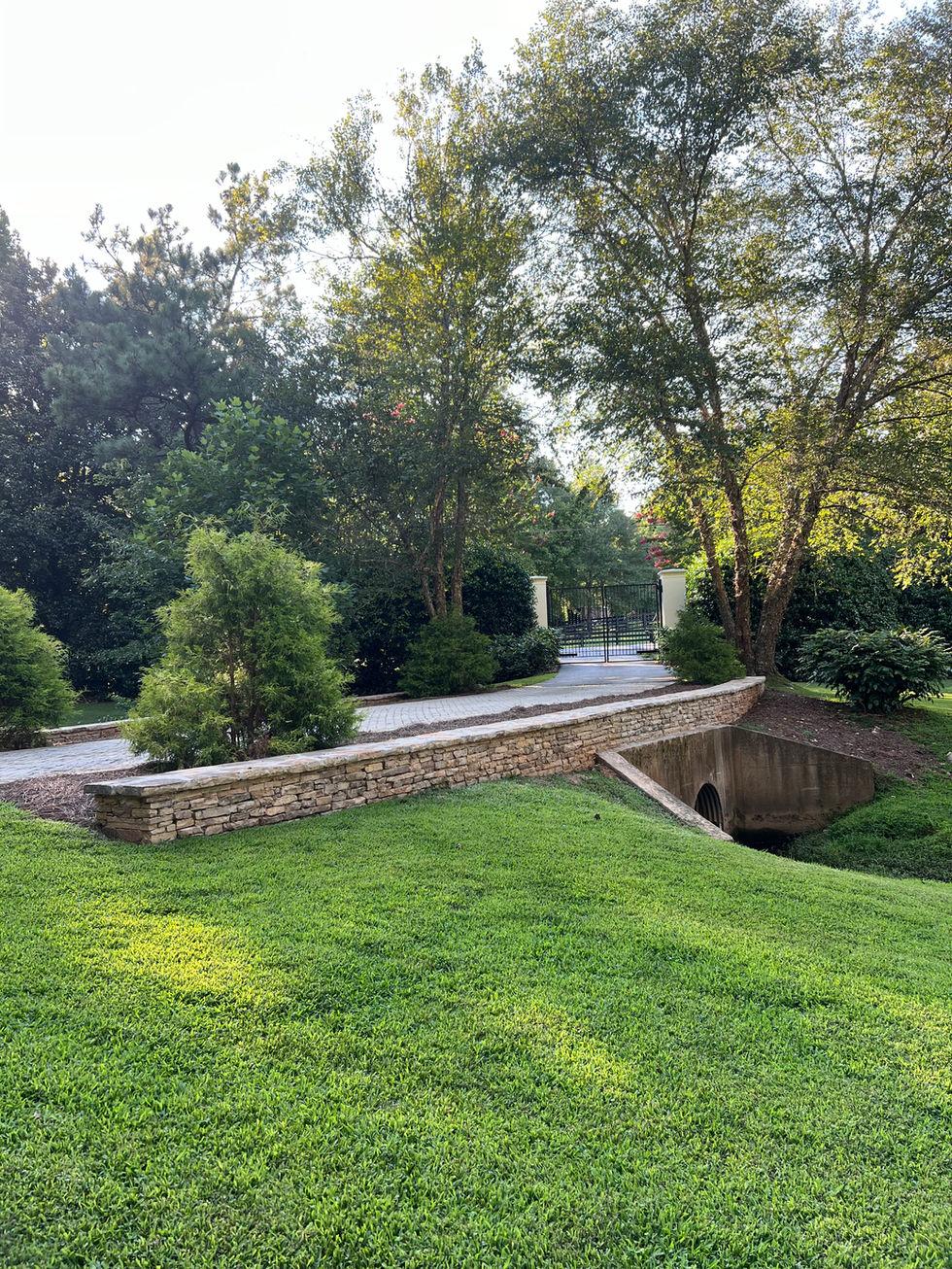 a stone wall along the side of a driveway leads to a gate