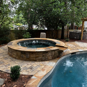 a stone hot tub sits next to a swimming pool