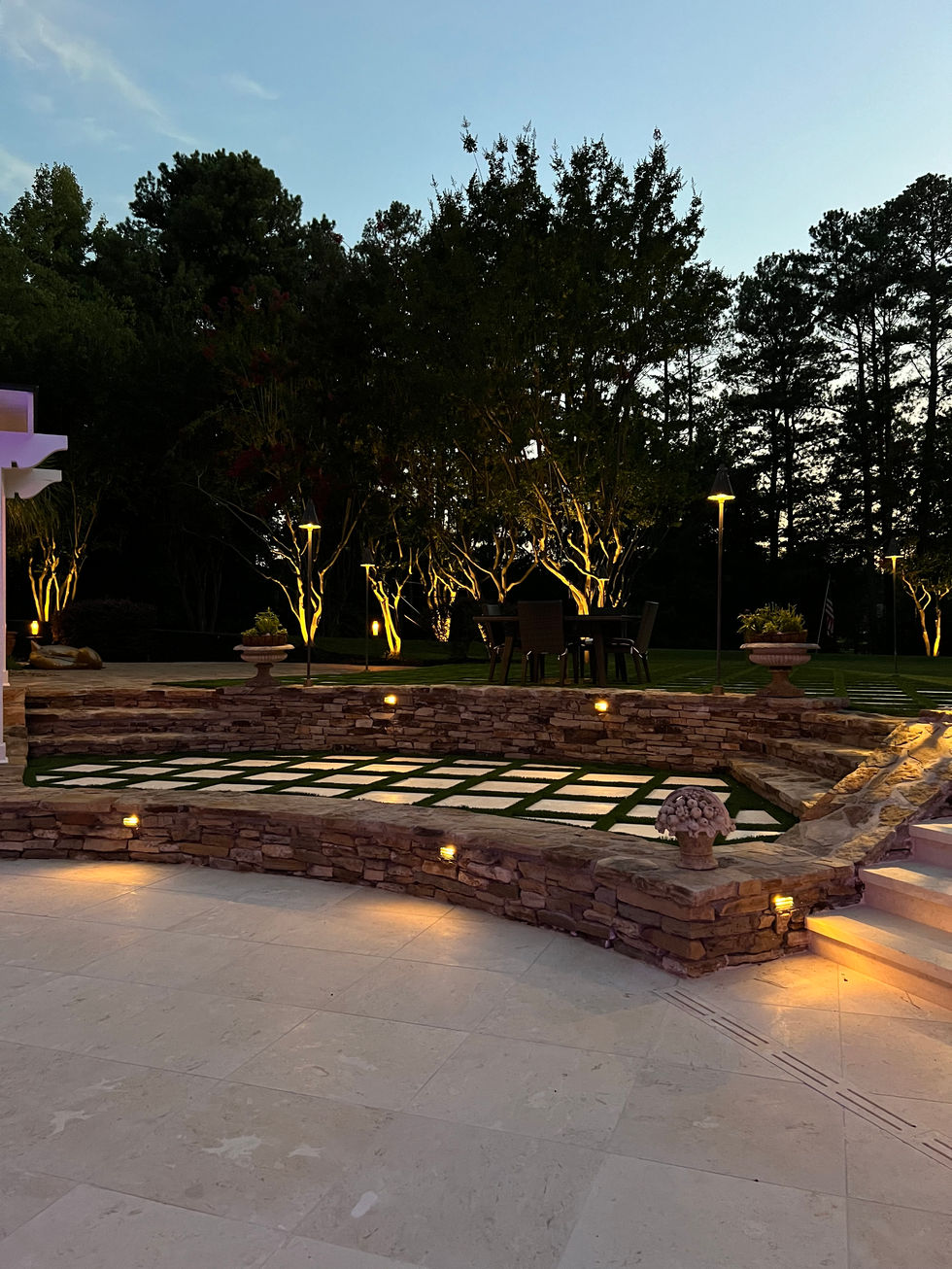 a patio area with a stone wall and trees lit up at night