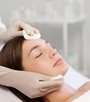 Young woman having facial beauty treatment, beautician cleaning and touching female face w