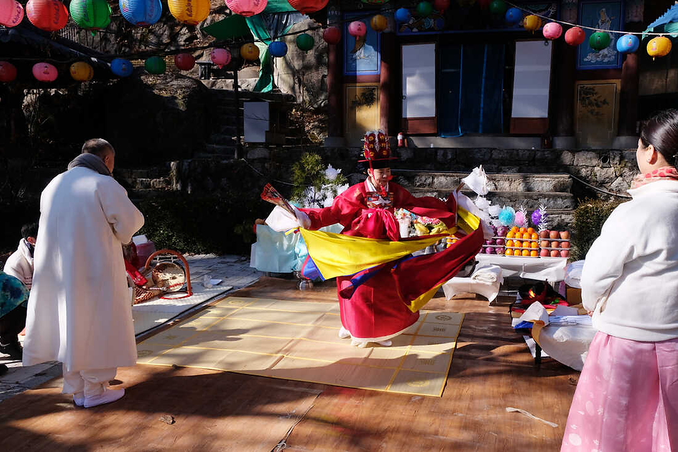 Colorful gut ritual in progress with a shaman in red robes dancing in front of an altar and onlookers