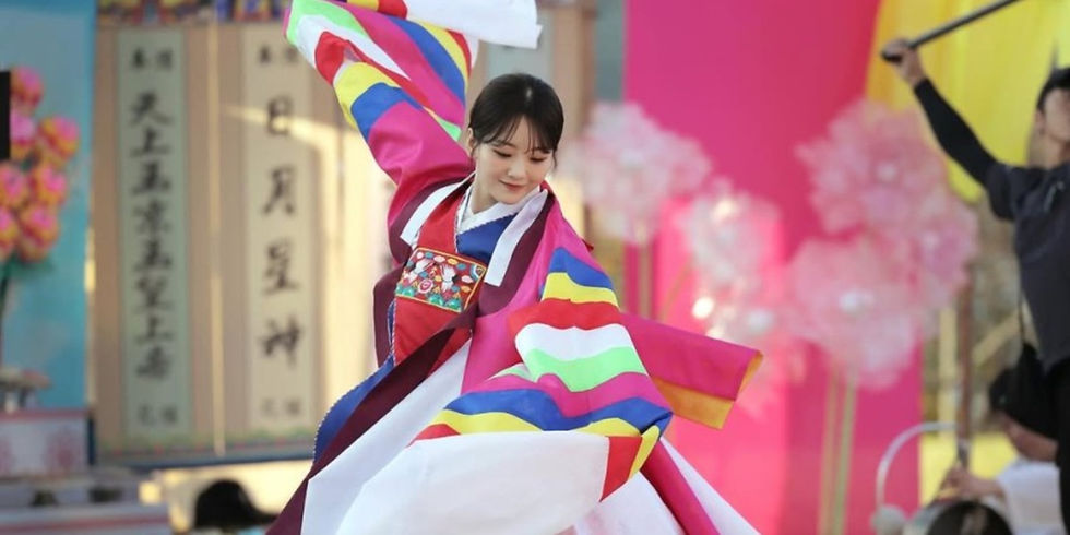 Korean actress Cho Yi-hyun wearing a bright traditional hanbok, dancing during a colorful shamanic ceremony scene from Head Over Heels